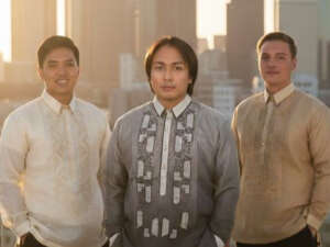 Three men wearing modern Barong Tagalogs on a city rooftop at sunset.