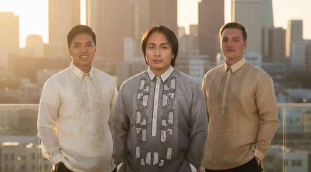 Three men wearing modern Barong Tagalogs on a city rooftop at sunset.